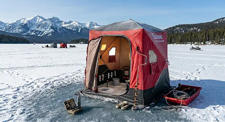A high-quality photorealistic portable ice shanty set up on a frozen Canadian lake with snow-capped mountains in the background. portable ice shanties