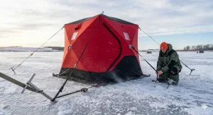 A flip-over ice shelter being towed by a snowmobile across a frozen lake for mobile ice fishing.