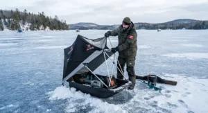 An angler setting up a flip-over sled ice fishing shelter on a frozen Canadian lake.