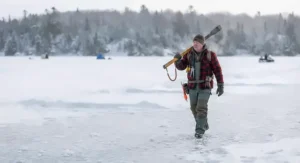 An outdoors person carrying an ice chisel for safety while walking across a frozen Canadian bay.